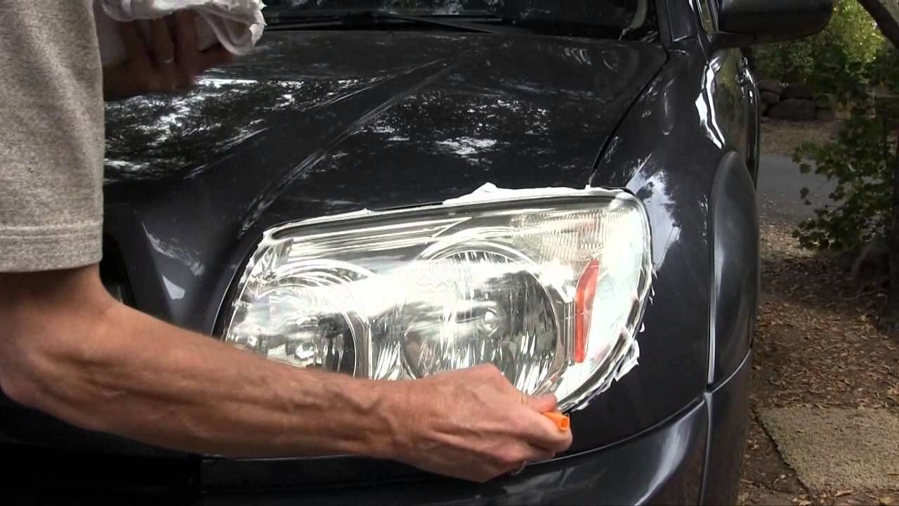Pulido a mano de un faro con crema y paño sobre un auto gris oscuro